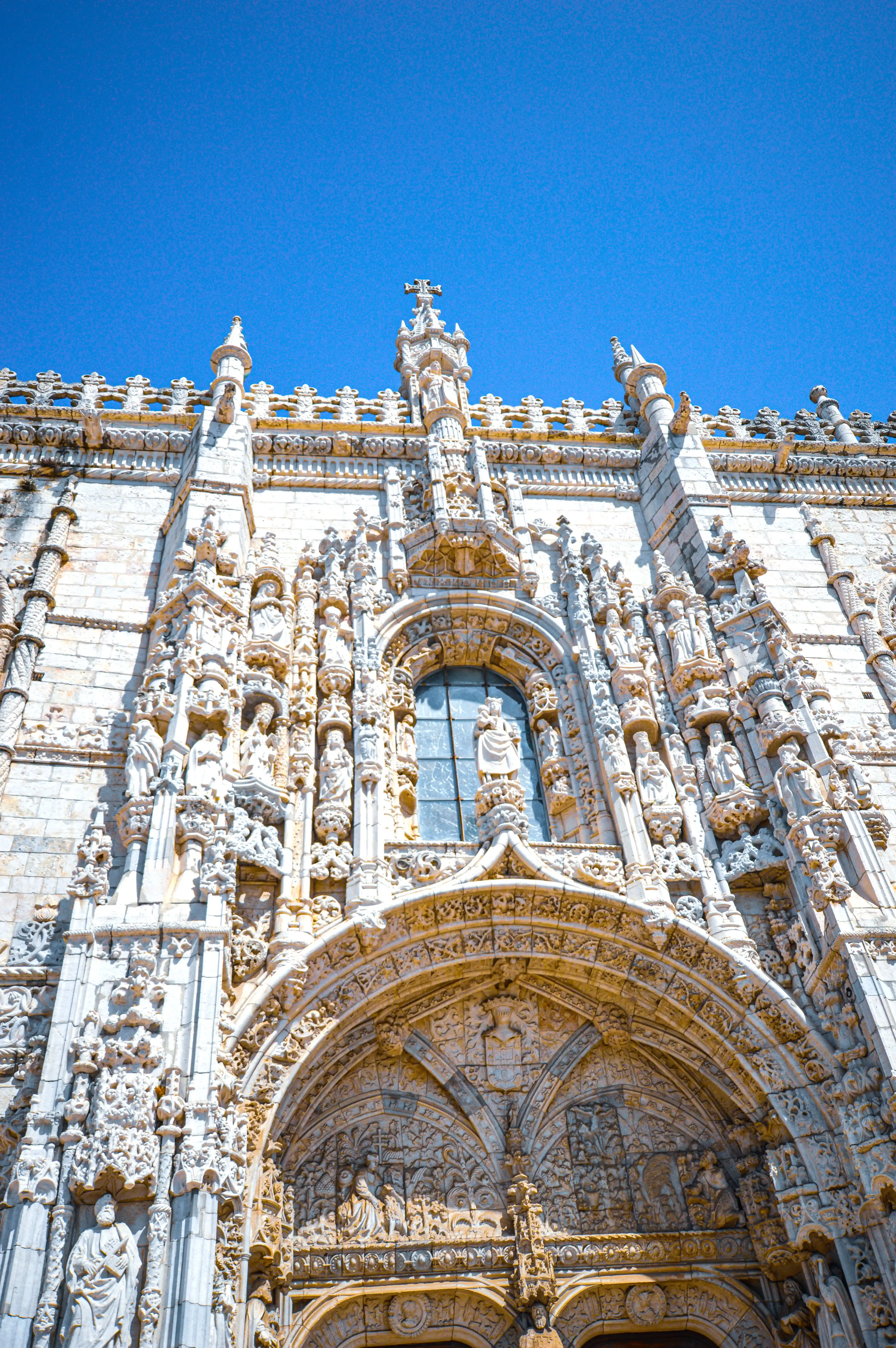 Close-up view of an ornate white stone Gothic building facade with detailed sculptures and arches against a bright blue sky.